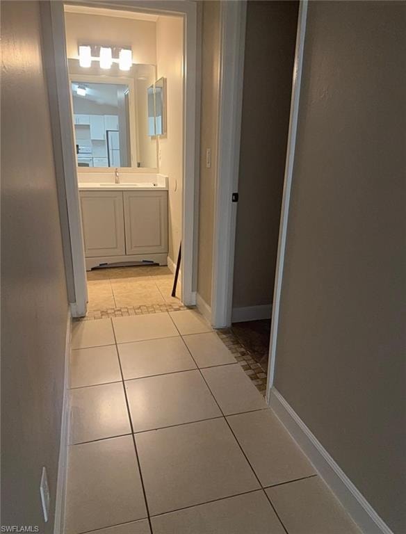 Hallway featuring large square tile flooring, leading to a bathroom with a vanity and a rectangular mirror