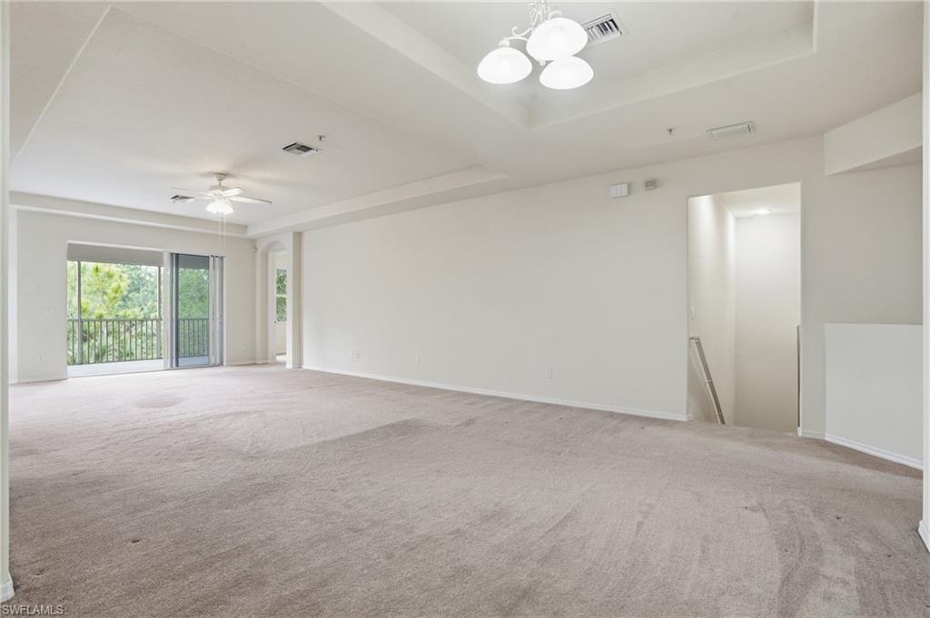 Empty room with a raised ceiling, a chandelier, carpet flooring, and ceiling fan