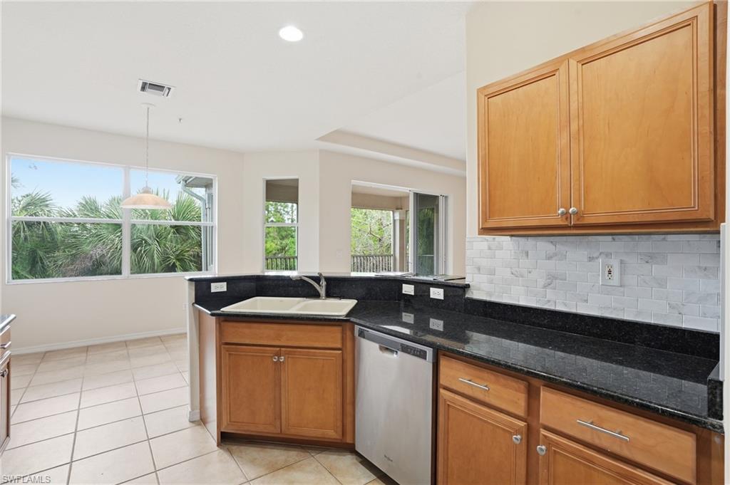Kitchen featuring stainless steel dishwasher, dark stone countertops, wood finish cabinets, and hanging light fixtures