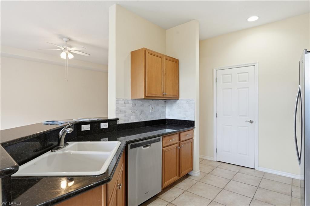 Kitchen with stainless steel appliances, ceiling fan, backsplash, light tile patterned floors, and dark stone countertops