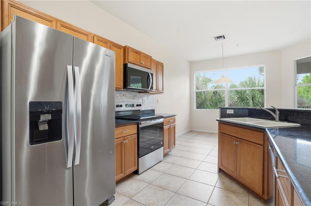 Kitchen featuring stainless steel appliances, wood finish cabinets, pendant lighting, and decorative backsplash