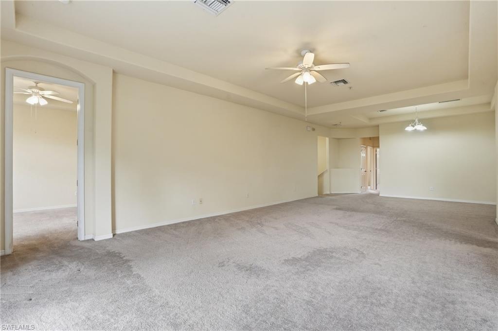 Empty room with a ceiling fan, a tray ceiling, and light colored carpet