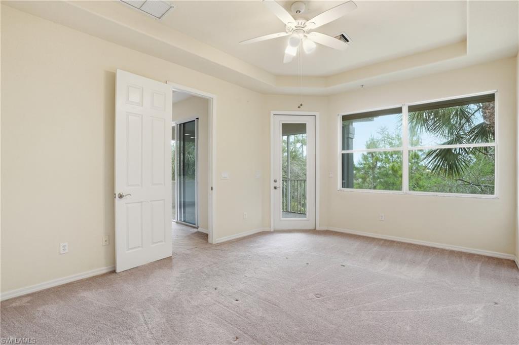 Unfurnished room featuring a raised ceiling, light carpet, and a ceiling fan