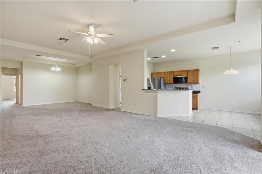 Unfurnished living room featuring a raised ceiling, ceiling fan, light carpet, and recessed lighting
