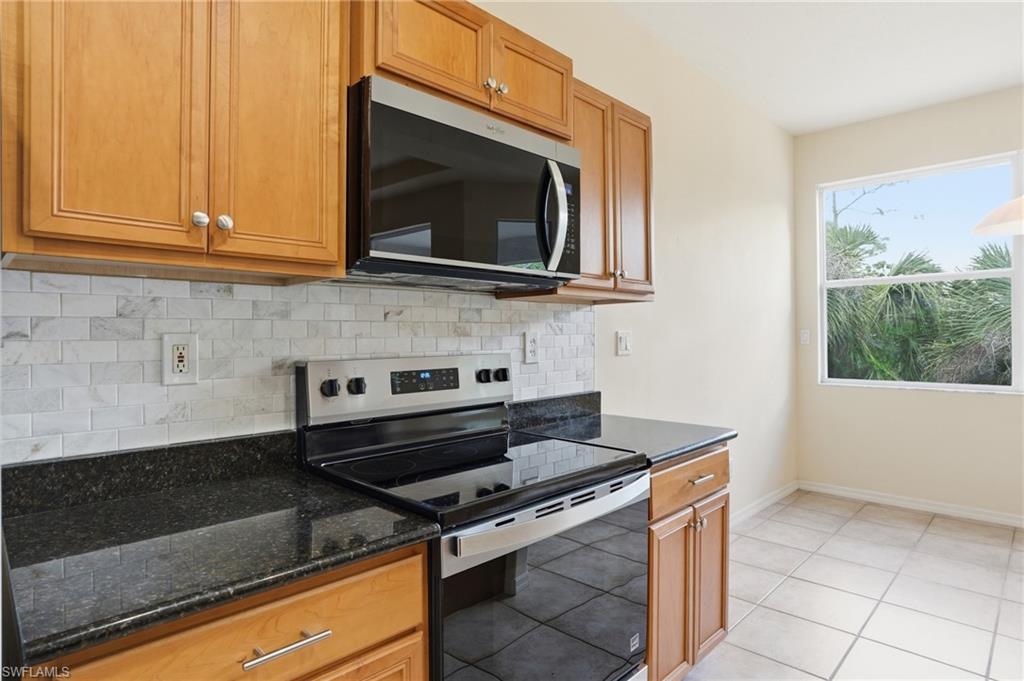 Kitchen with stainless steel appliances, tasteful backsplash, dark stone counters, wood finish cabinetry, and light tile patterned floors