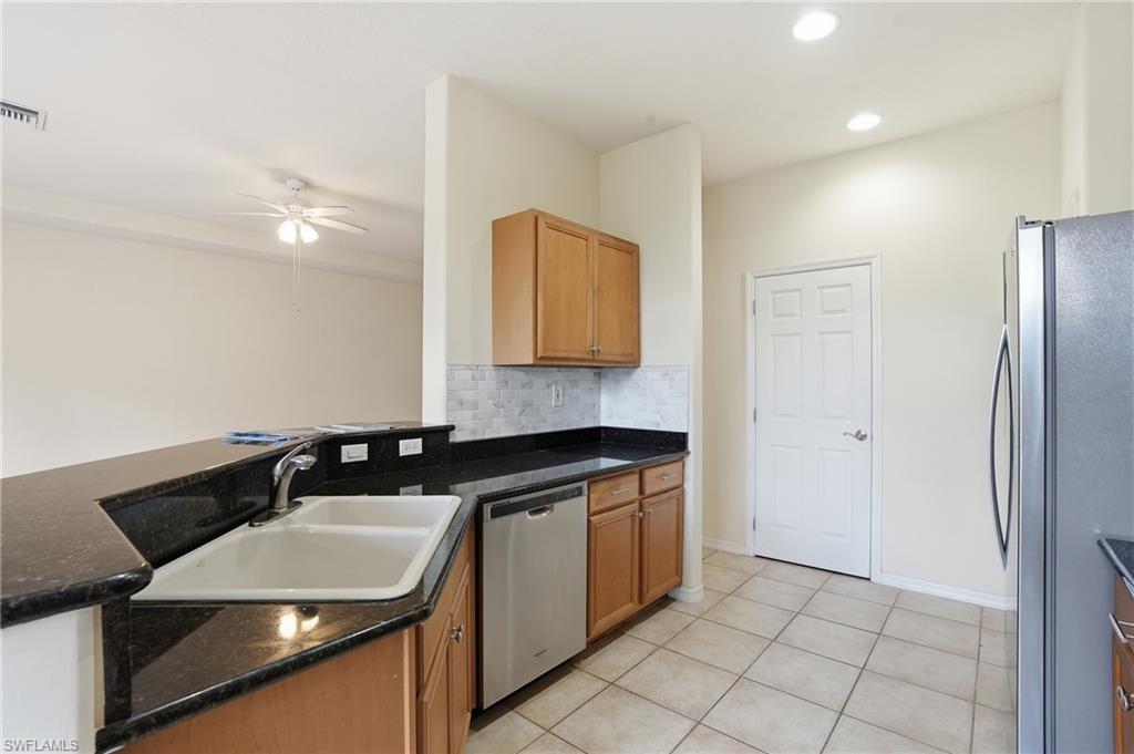 Kitchen with stainless steel appliances, decorative backsplash, a ceiling fan, light tile patterned floors, and dark stone counters