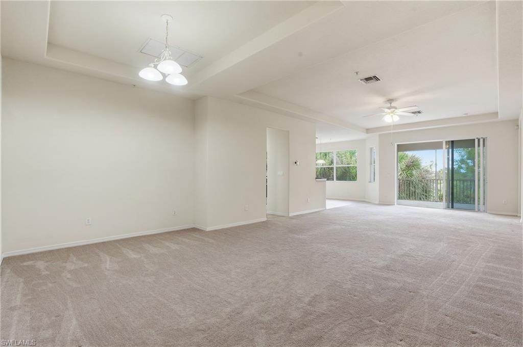 Unfurnished room featuring a raised ceiling, light carpet, and a ceiling fan