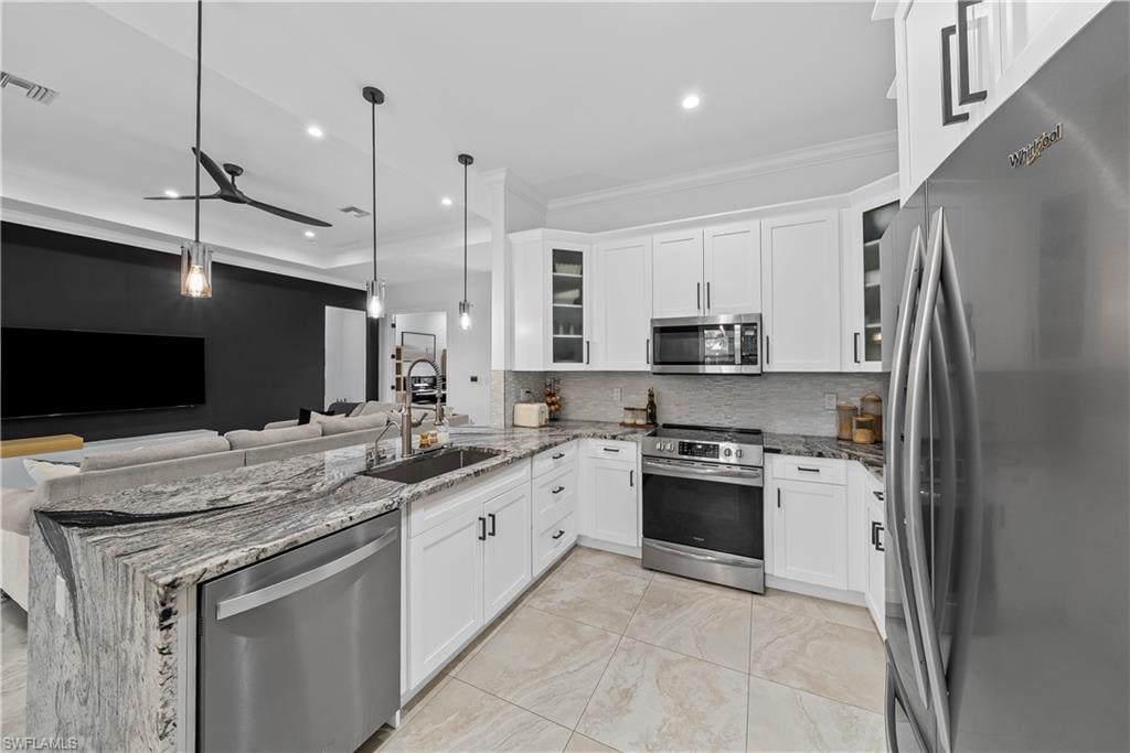 Kitchen with stainless steel appliances, light stone counters, white cabinetry, a peninsula, and crown molding