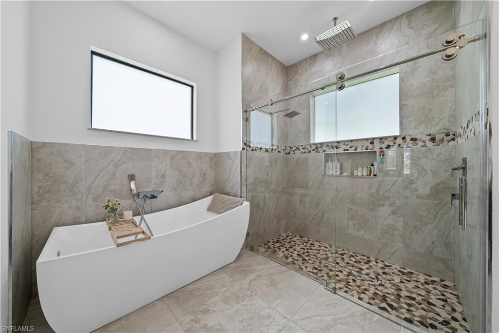 Bathroom featuring tile walls, a shower stall, a freestanding tub, and light marble finish floors