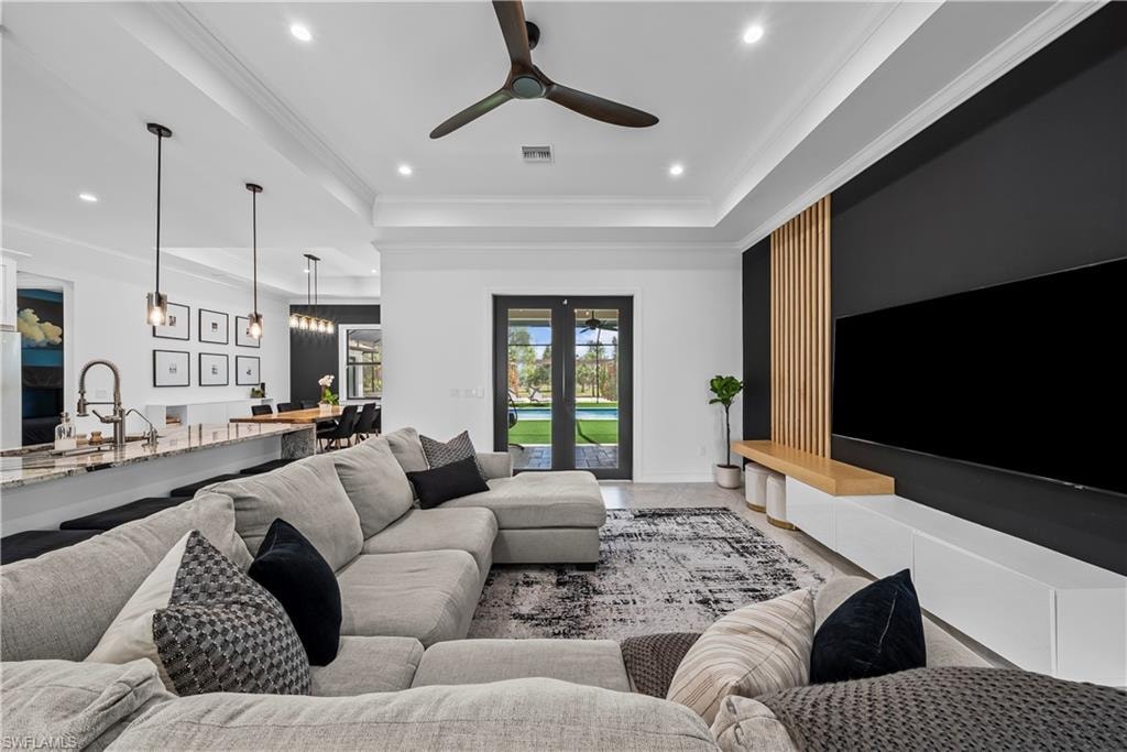 Living room featuring french doors, ceiling fan, ornamental molding, recessed lighting, and a tray ceiling
