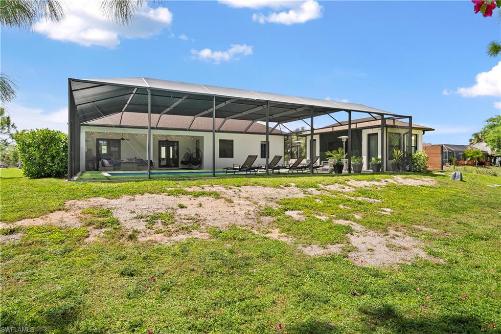 Rear view of property with a sunroom, glass enclosure, a yard, and an outdoor pool