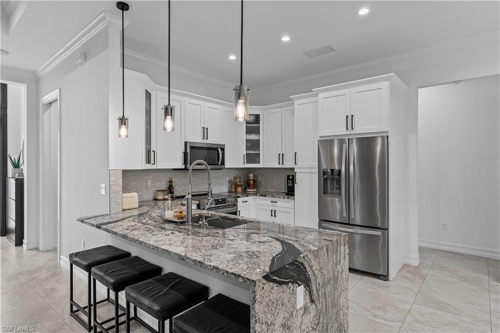 Kitchen featuring a breakfast bar area, dark stone countertops, stainless steel appliances, glass fronted cabinets, and a peninsula
