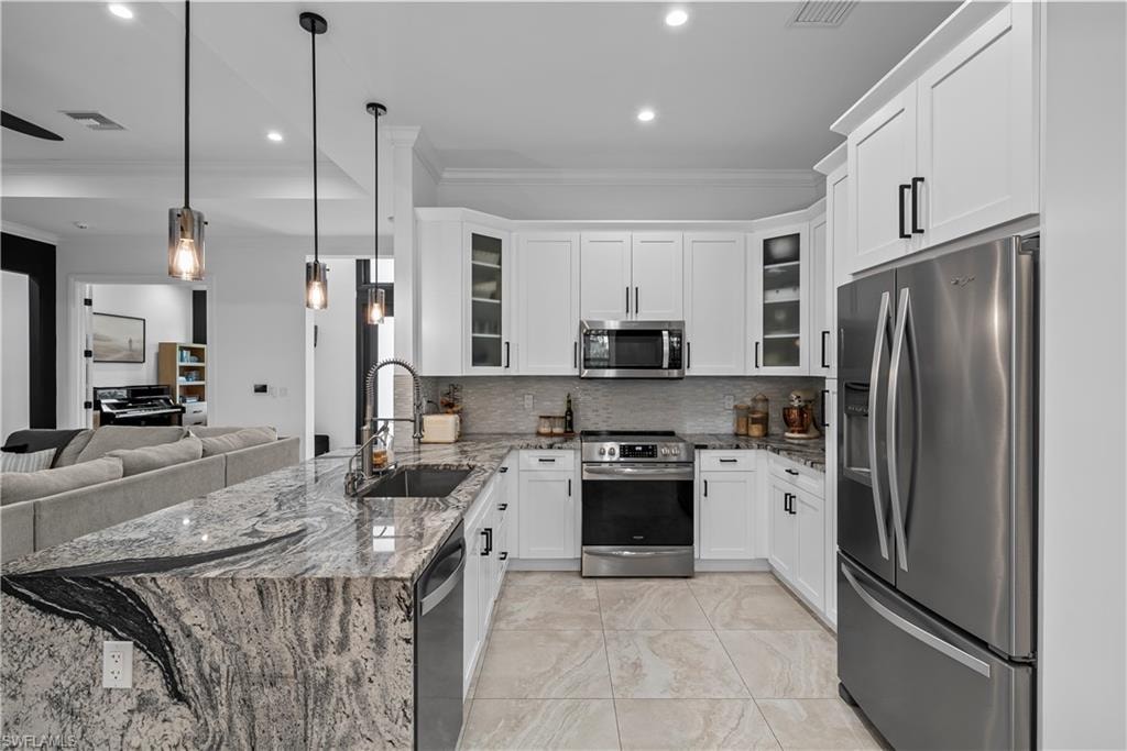 Kitchen featuring dark stone counters, ornamental molding, stainless steel appliances, a peninsula, and white cabinetry