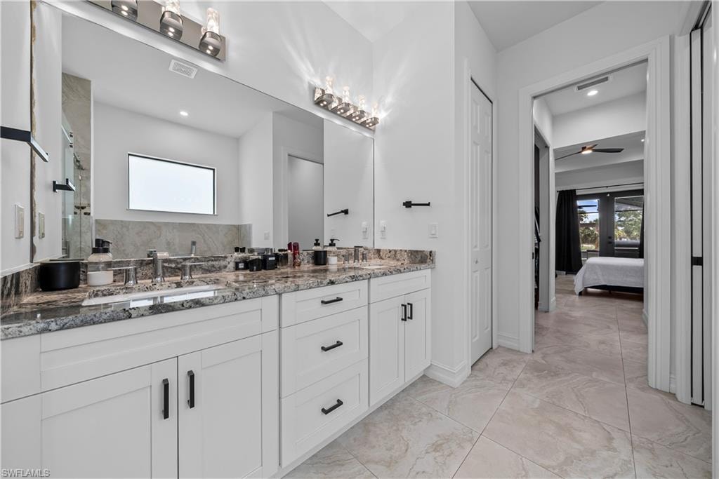 Ensuite bathroom with a closet, double vanity, light marble finish floors, and tiled shower