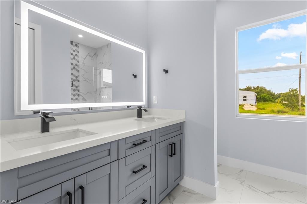 Full bathroom with light marble finish floors, double vanity, plenty of natural light, and a shower