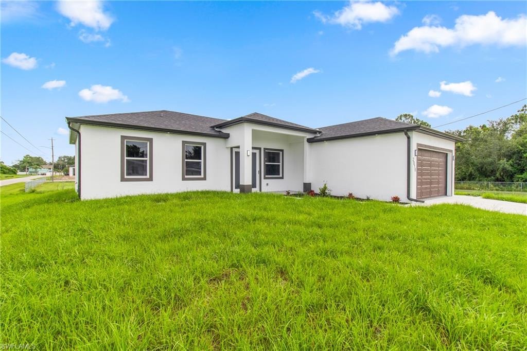 Prairie-style house with a garage, driveway, stucco siding, and a front lawn