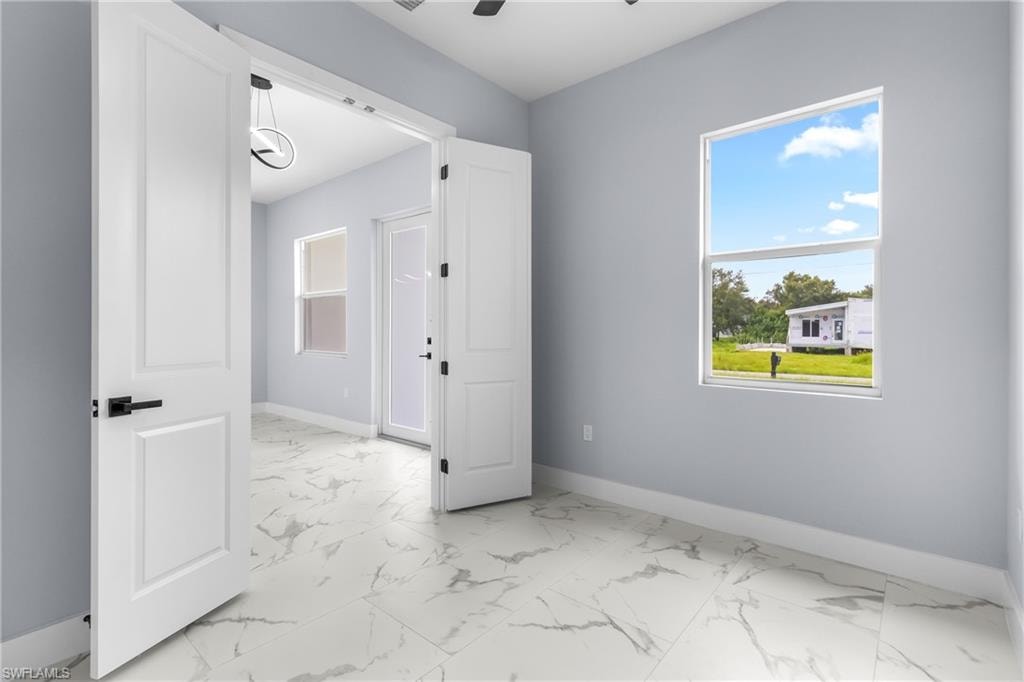 Empty room with healthy amount of natural light, light marble finish floors, and a ceiling fan