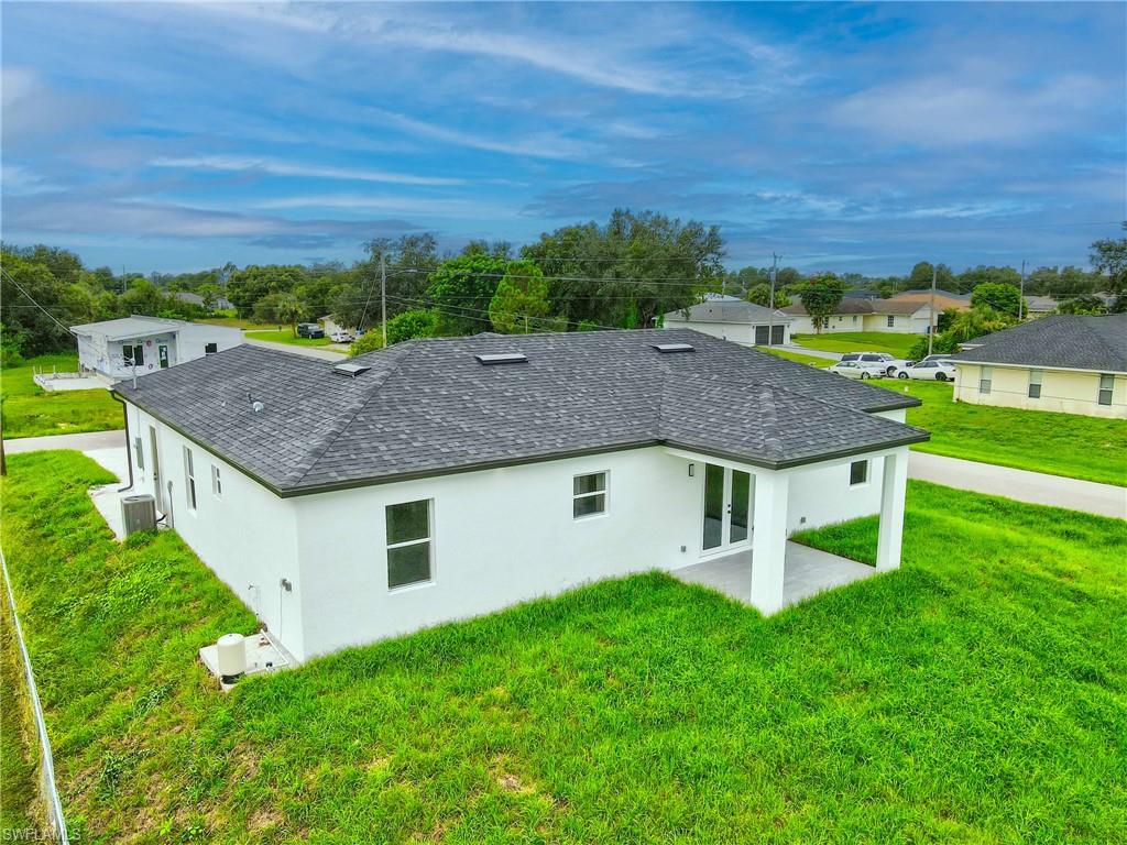 Back of house with roof with shingles, a yard, and stucco siding
