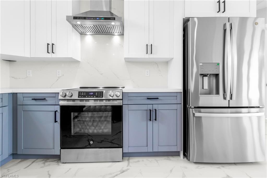 Kitchen featuring appliances with stainless steel finishes, white cabinets, and light marble finish flooring