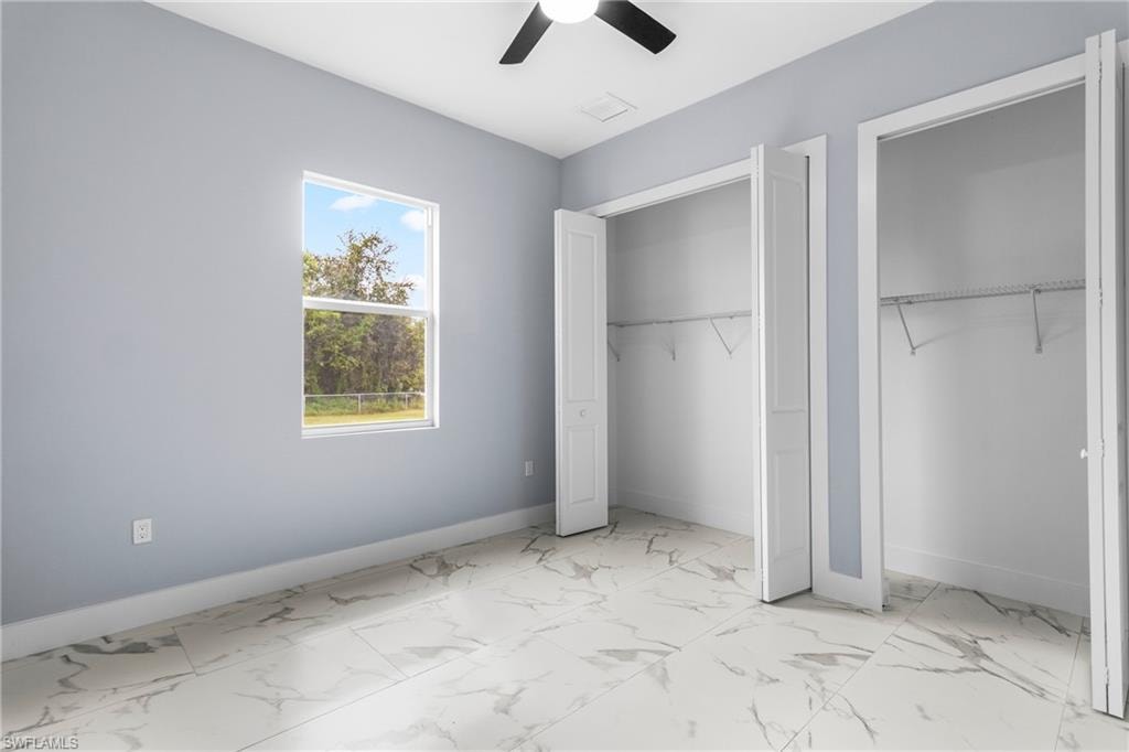 Unfurnished bedroom featuring light marble finish flooring, two closets, and ceiling fan