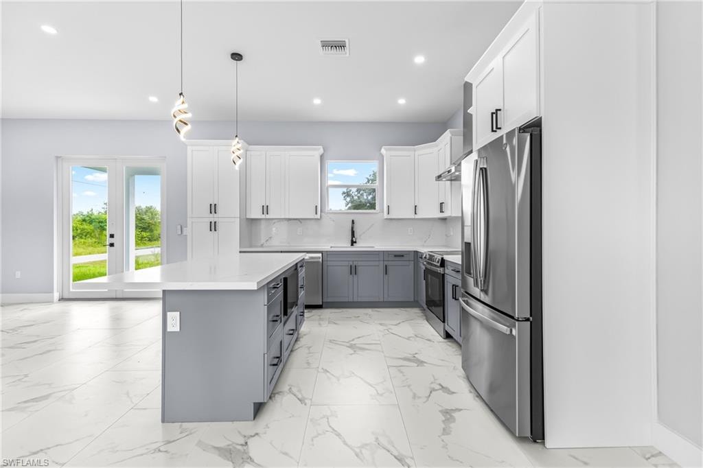 Kitchen with gray cabinetry, white cabinets, appliances with stainless steel finishes, hanging light fixtures, and tasteful backsplash