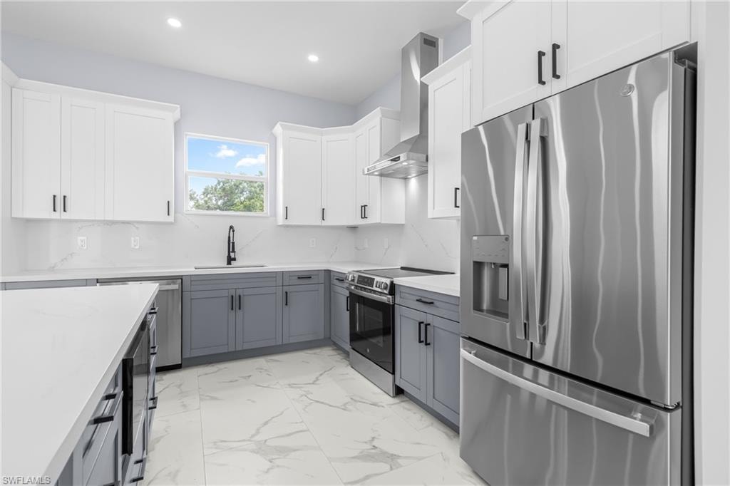 Kitchen with stainless steel appliances, white cabinets, gray cabinetry, backsplash, and light stone countertops