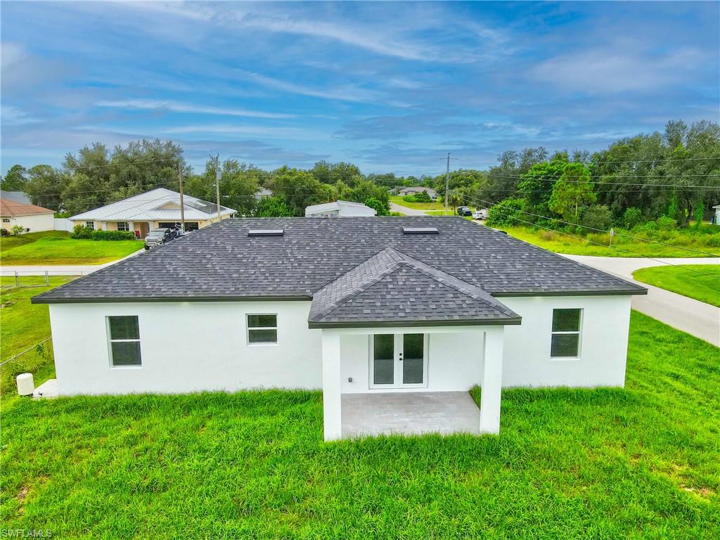 Back of house featuring a shingled roof, a yard, stucco siding, and french doors