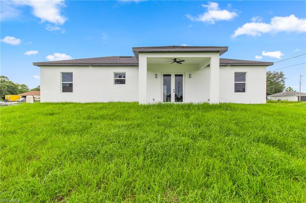 Rear view of property featuring ceiling fan, stucco siding, a patio area, french doors, and a yard