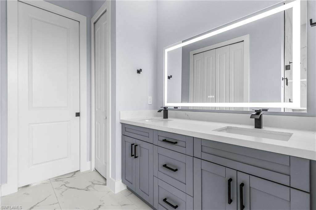 Bathroom featuring light marble finish floors, double vanity, and a closet