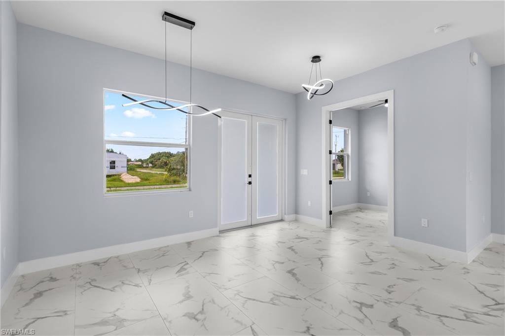 Unfurnished dining area featuring light marble finish floors, a chandelier, and french doors