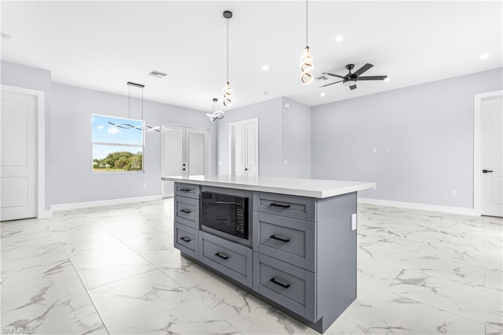 Kitchen featuring a ceiling fan, decorative light fixtures, a center island, black microwave, and light marble finish floors
