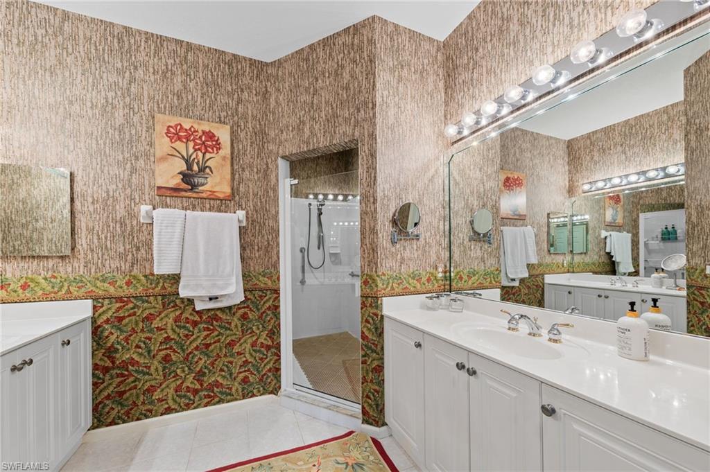 Full bathroom featuring two vanities, wallpapered walls, light tile patterned flooring, and a stall shower