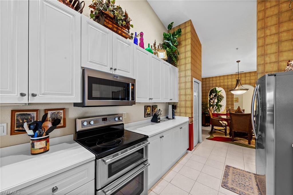 Kitchen featuring stainless steel appliances, wallpapered walls, light countertops, white cabinets, and hanging light fixtures