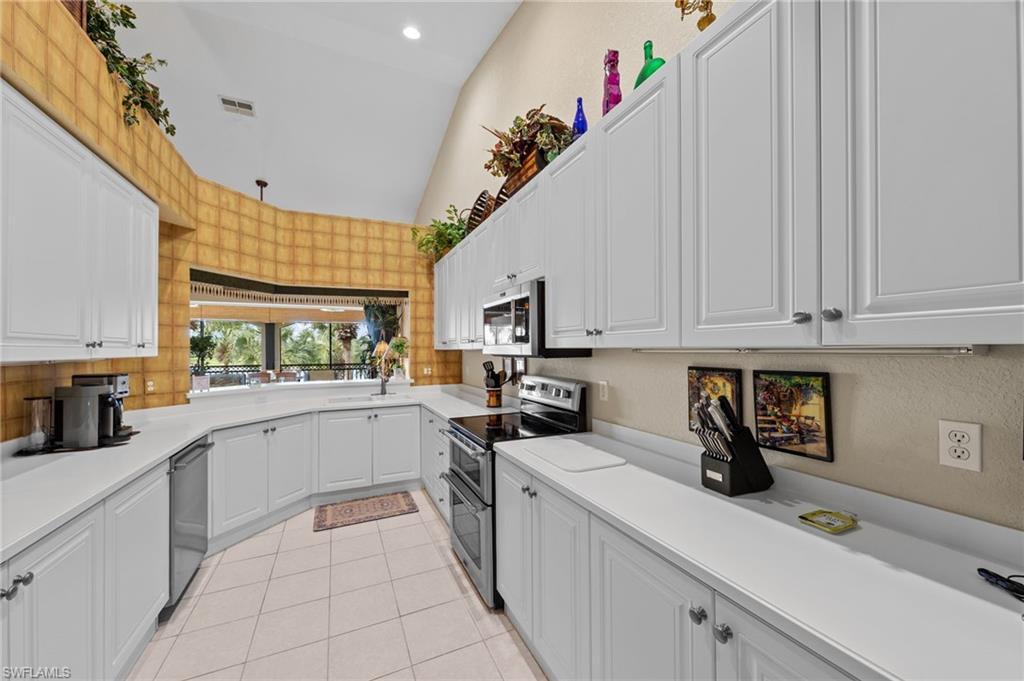 Kitchen featuring white cabinets, stainless steel appliances, lofted ceiling, and recessed lighting