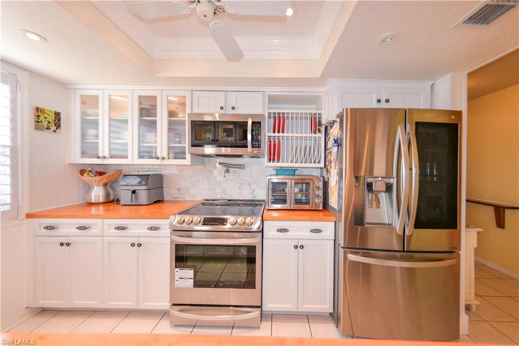 Modern kitchen featuring white cabinetry, stainless steel appliances, marble-look backsplash, wood-finish countertops, and recessed lighting