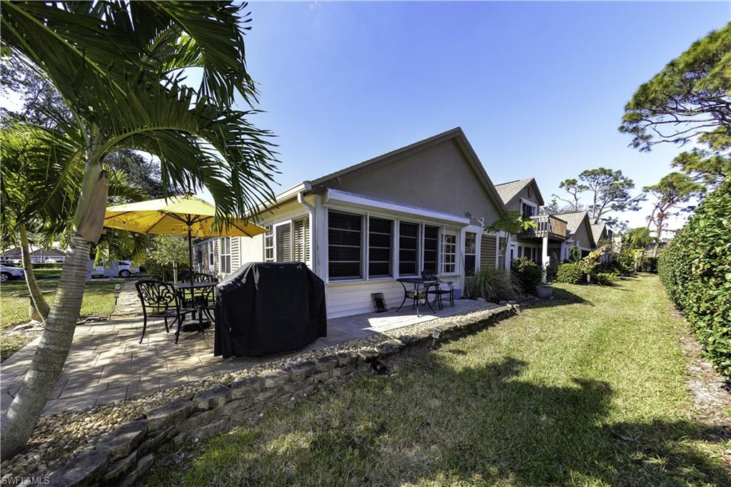 Exterior featuring a paver patio, mature palm trees, a spacious lawn, and a low stone retaining wall