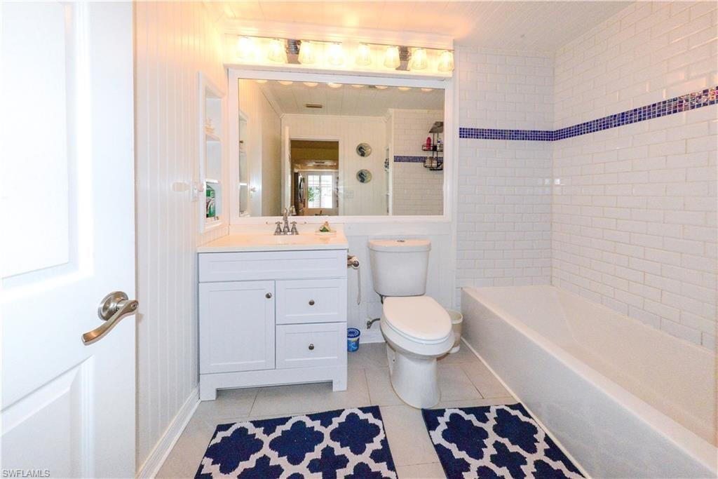 Bathroom featuring a white vanity with integrated sink, a rectangular mirror, a light fixture with four bulbs, white subway tile walls with a blue accent band, and a white bathtub