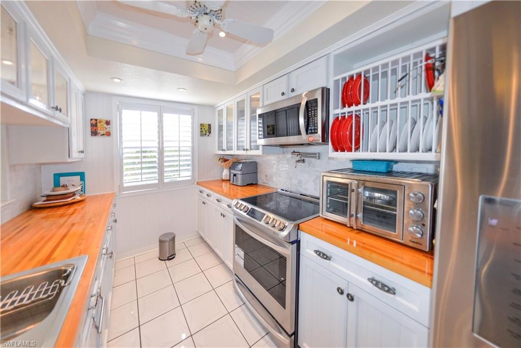 Bright kitchen featuring white cabinetry, wood-finish countertops, stainless steel appliances, and tile flooring