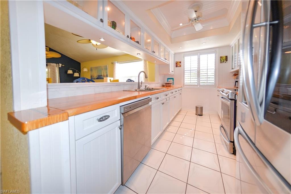 Galley kitchen featuring white cabinetry with brushed nickel hardware, wood-finish countertops, stainless steel appliances, and a pass-through window