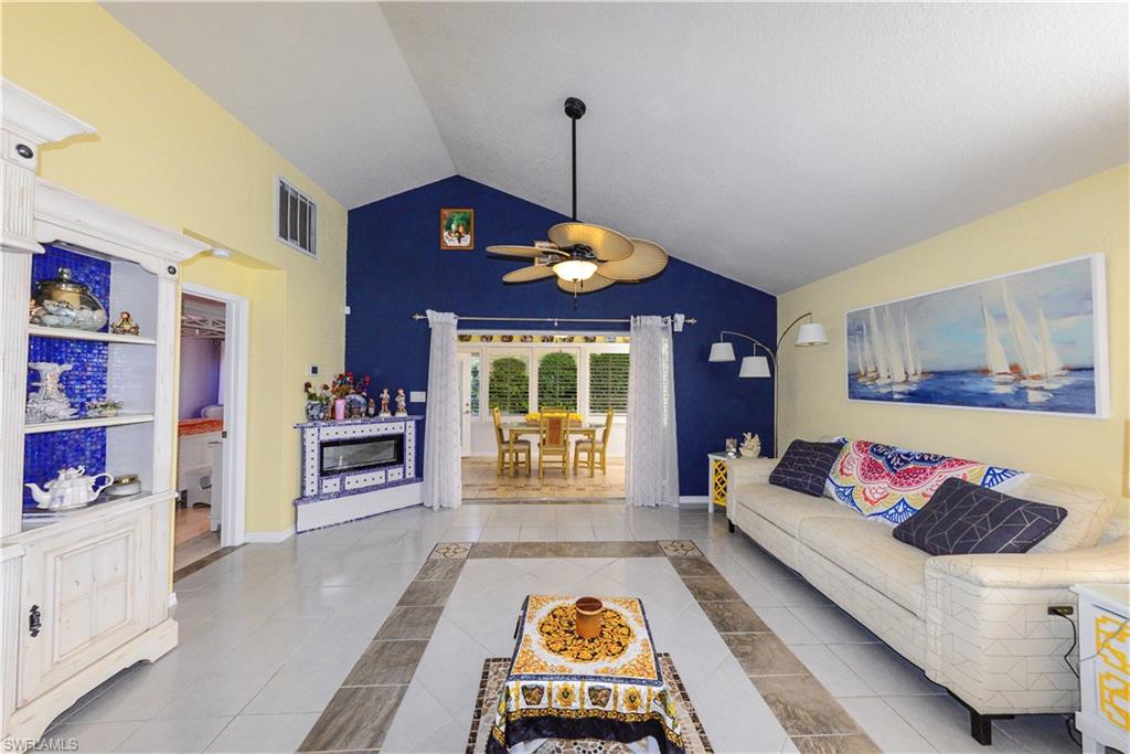 Vaulted ceiling living area featuring tile flooring, a built-in electric fireplace, and an exposed beam ceiling fan