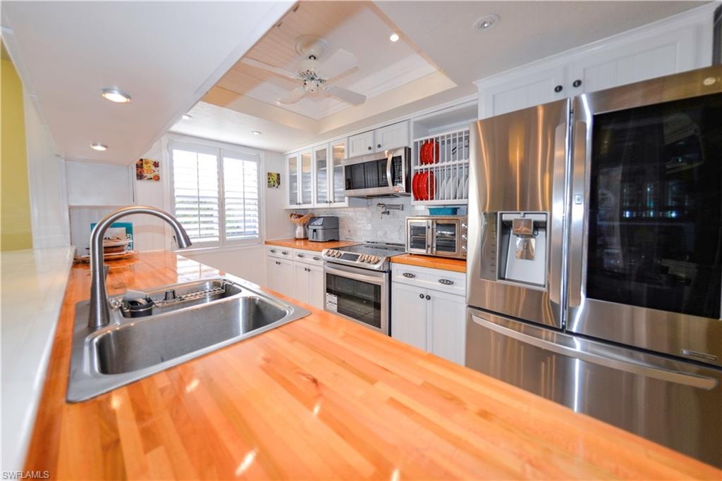 Kitchen featuring wood-finish countertops, stainless steel appliances, white cabinetry, a dual-basin sink with a gooseneck faucet, and shuttered window coverings