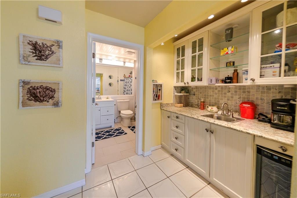 White cabinetry with granite-style countertops, stainless steel sink, and mosaic tile backsplash