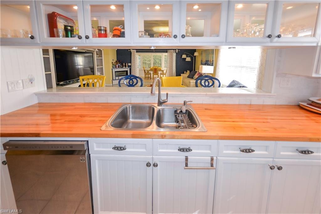 Kitchen featuring a stainless steel double basin sink, light wood-finish countertops, and white paneled cabinetry with dark hardware