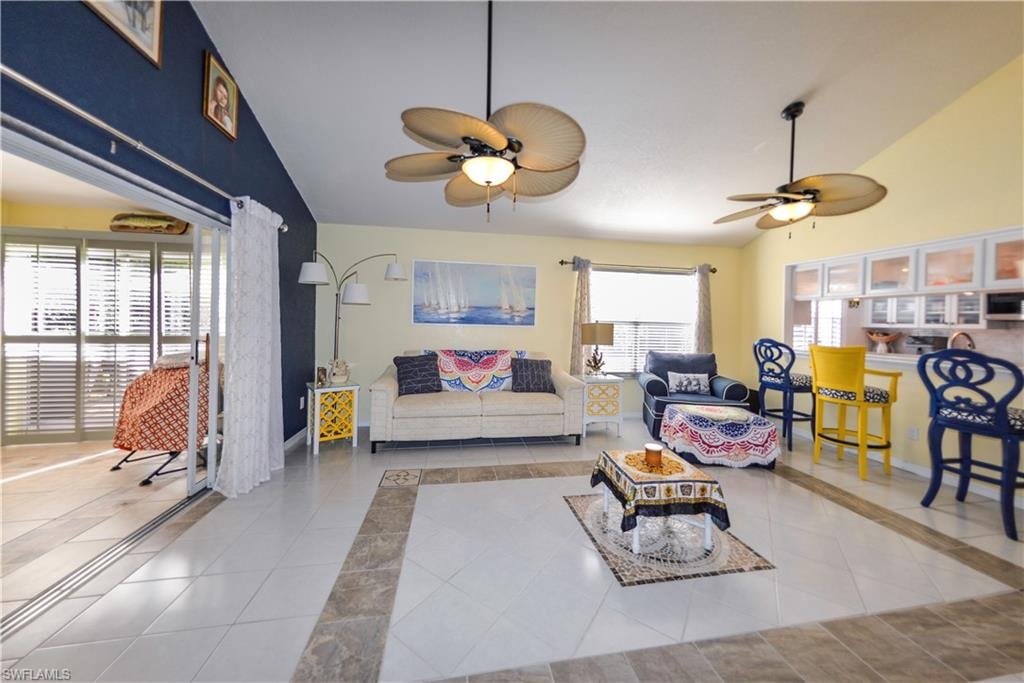 Spacious living area featuring tile flooring with decorative inlay, vaulted ceilings, and dual ceiling fans with integrated lighting