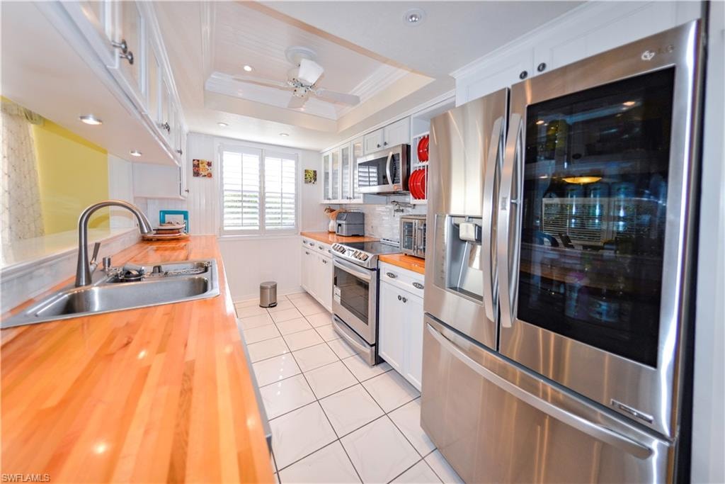 Modern kitchen featuring stainless steel appliances, wood-finish countertops, white cabinetry, a built-in microwave, and recessed lighting