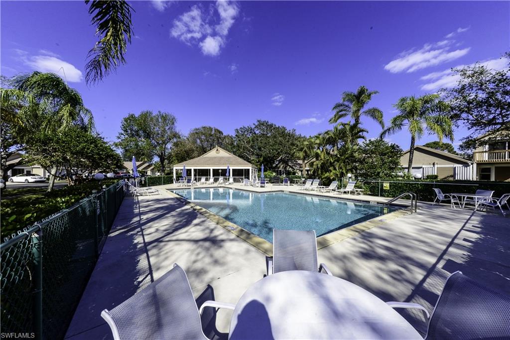 Community swimming pool with a surrounding concrete deck, flanked by mature palm trees and lush greenery