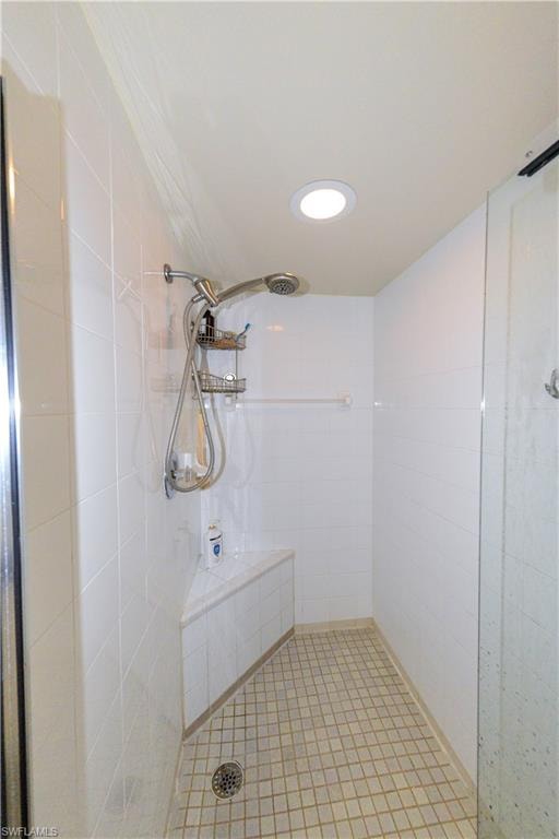 Walk-in shower featuring white tile walls, a built-in corner bench, square mosaic floor tiles, a recessed ceiling light, and a handheld shower fixture