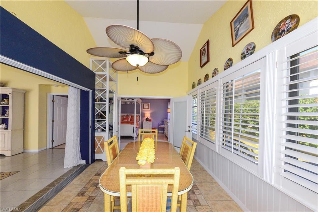 Sunroom dining area featuring vaulted ceilings, a ceiling fan, and tile flooring