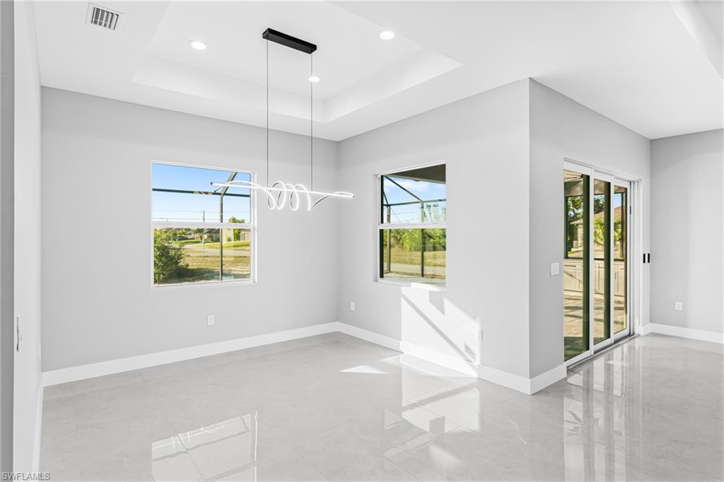 Empty room with healthy amount of natural light, a tray ceiling, recessed lighting, and a chandelier
