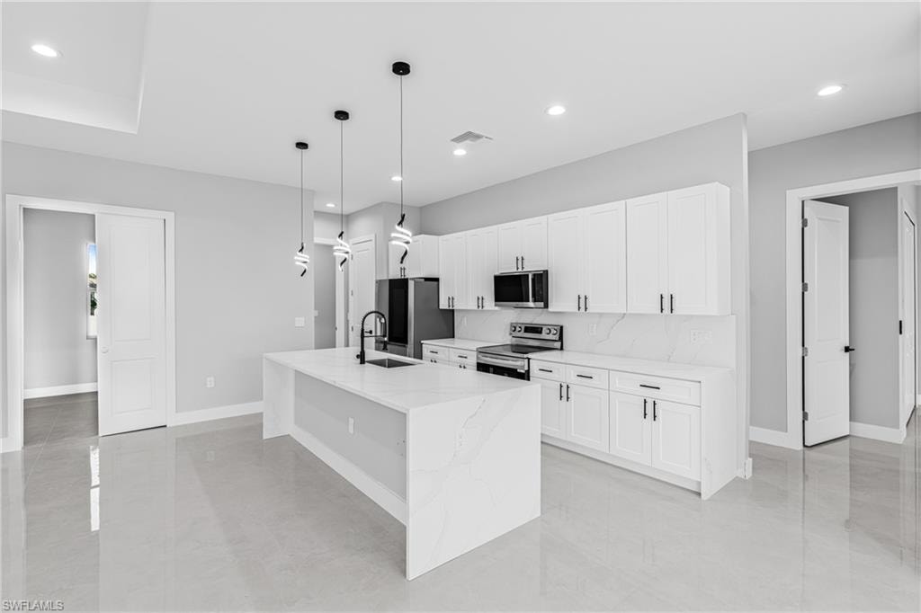 Kitchen featuring appliances with stainless steel finishes, light stone countertops, decorative light fixtures, white cabinetry, and a center island with sink